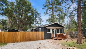 A cabin with a gravel driveway, wooden deck, and a fenced yard surrounded by tall pine trees. - The Maple Lane Hideaway (Sugarloaf)