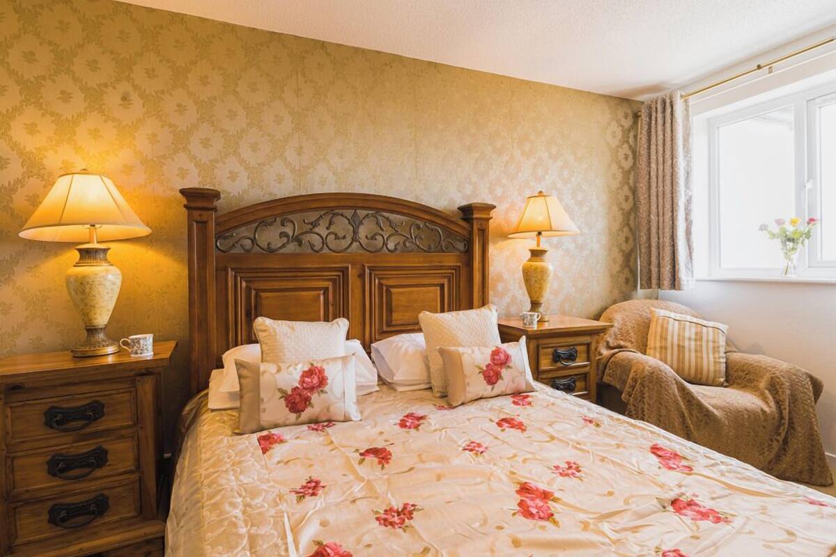 A neatly made bed with floral bedding, two bedside lamps, a wooden nightstand with drawers, and a window with curtains.