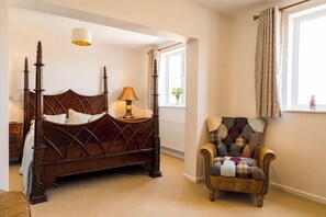 A bedroom with a wooden four-poster bed, a lamp, a plaid armchair, and a window with curtains. - Hawk and Buckle Inn (Llannefydd)