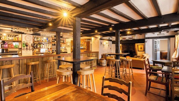 A bar area with wooden furniture, a bar counter, and shelves with bottles. - Hawk and Buckle Inn (Llannefydd)