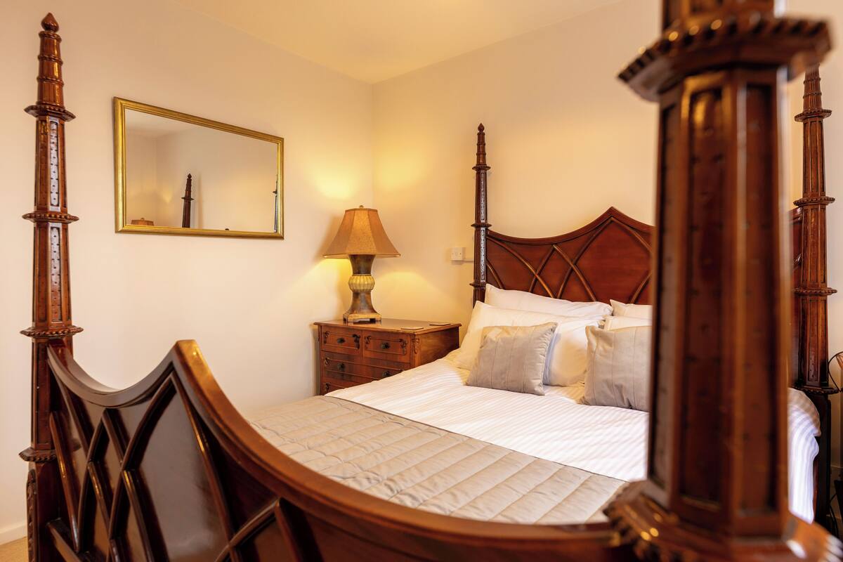 A traditional wooden bed with a headboard, a bedside table with a lamp, and a mirror on the wall.