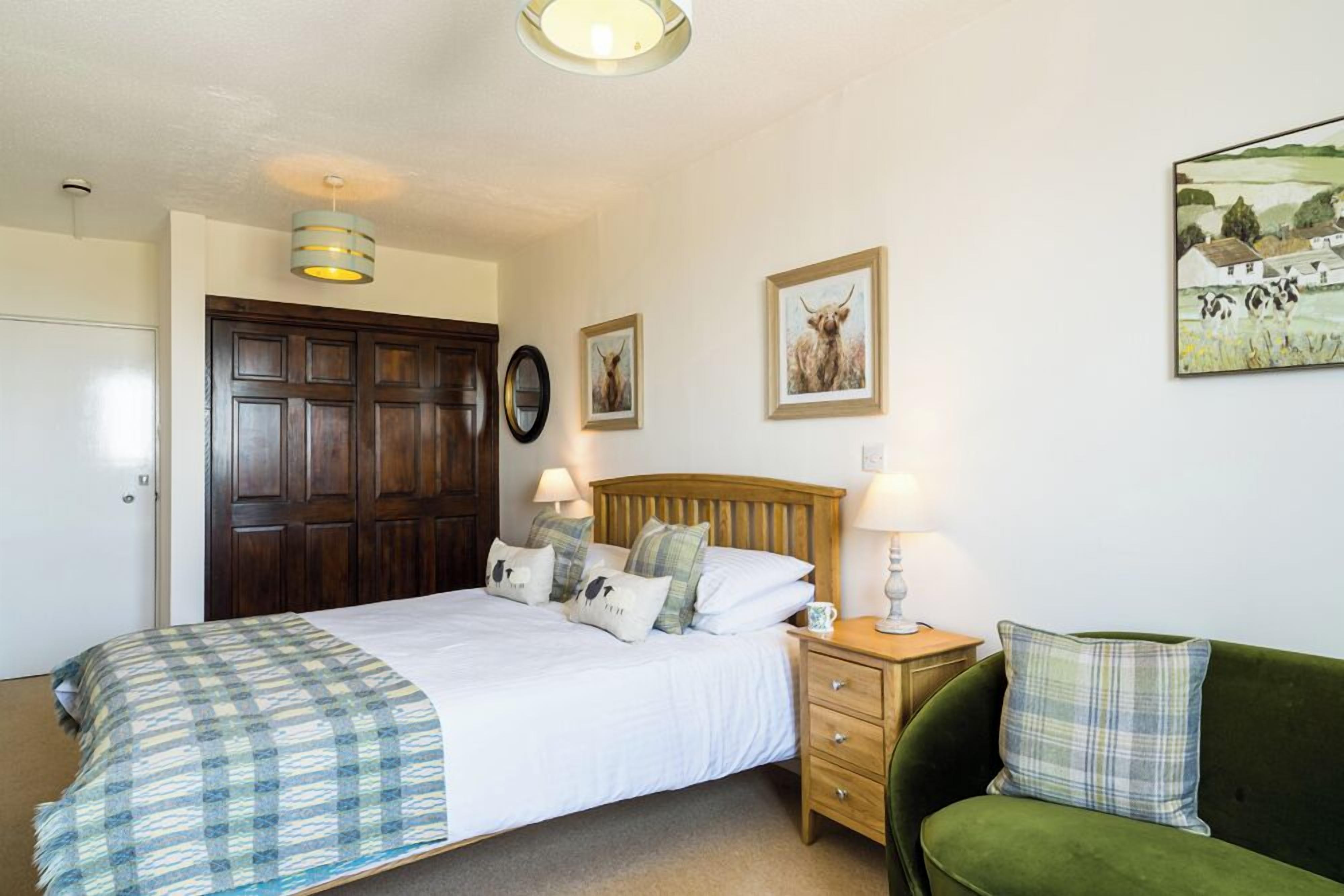 Un dormitorio con una cama de madera, un sofá verde, una mesita de noche con lámpara y decoración en la pared.