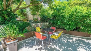 Een terras met een tafel en stoelen, omringd door weelderige begroeiing en een stenen muur.
