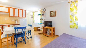 Een knus woongedeelte met kitchenette, een eethoek met blauwe stoelen, een televisie op een houten dressoir en een bed met paars sprei.
