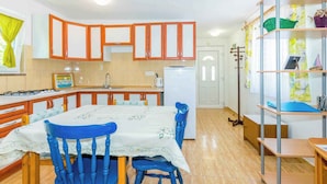 Een compacte keuken met houten kastjes, een eettafel met blauwe stoelen en een kleine koelkast.