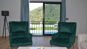 A room with two green velvet chairs, a white table with three candles, and a view of a pool and greenery through a glass door. - VILLA WITH LAKE AND FOREST VIEW IN DALYAN2 (Akcakavak)