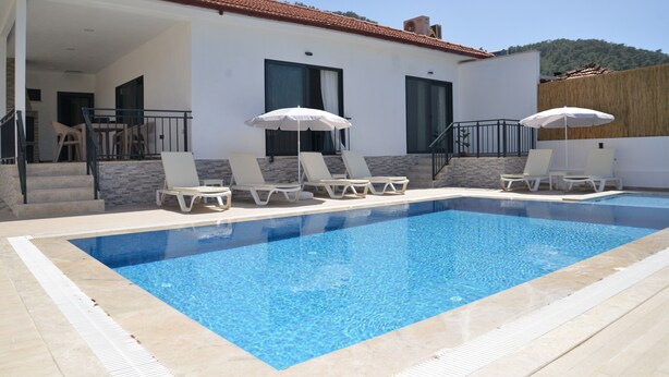 A swimming pool with lounge chairs and umbrellas, a covered patio area, and a view of a hilly landscape. - VILLA WITH LAKE AND FOREST VIEW IN DALYAN2 (Akcakavak)