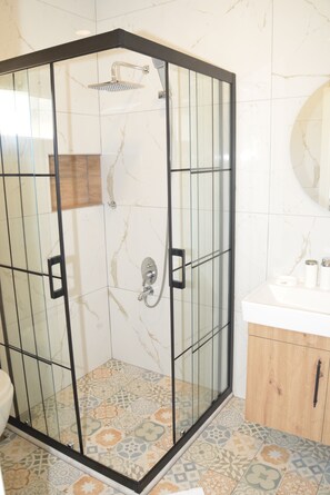 A walk-in shower with a glass door, a wooden cabinet, and a tiled floor.