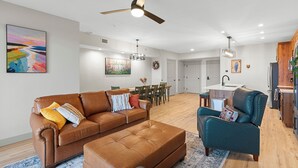 A modern living room with a brown leather sofa, a teal armchair, and a dining area with a wooden table and chairs.