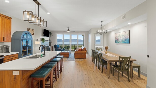 A modern kitchen with a large island, bar stools, a dining area with a wooden table and chairs, and a view of the mountains through large windows.