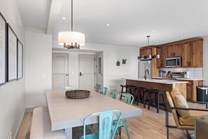Una cucina moderna con mobili in legno, un'isola centrale e un'area pranzo con un tavolo chiaro e sedie color verde acqua.