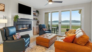 A living room with a fireplace, a television, a ceiling fan, and a view of the outdoors.