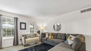 Una sala de estar con sofá, sillón, alfombra, lámpara y espejo.
