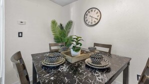 Un comedor con una mesa de mármol negro, dos sillas, un reloj y una planta en maceta.