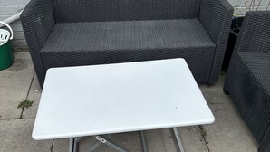 Une table blanche aux pieds métalliques, placée devant un canapé en osier foncé, le tout adossé à un mur de briques blanches.