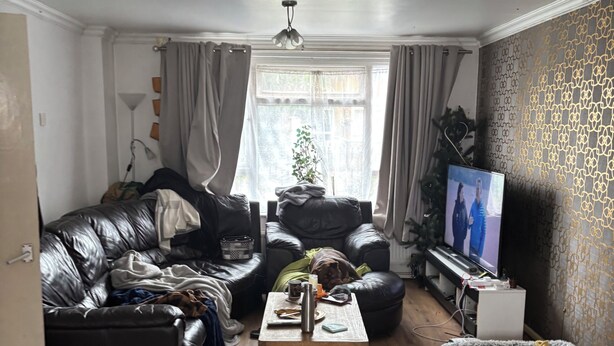 Un salon avec un canapé en cuir, une table basse en bois, un téléviseur et un mur décoré d’un motif.