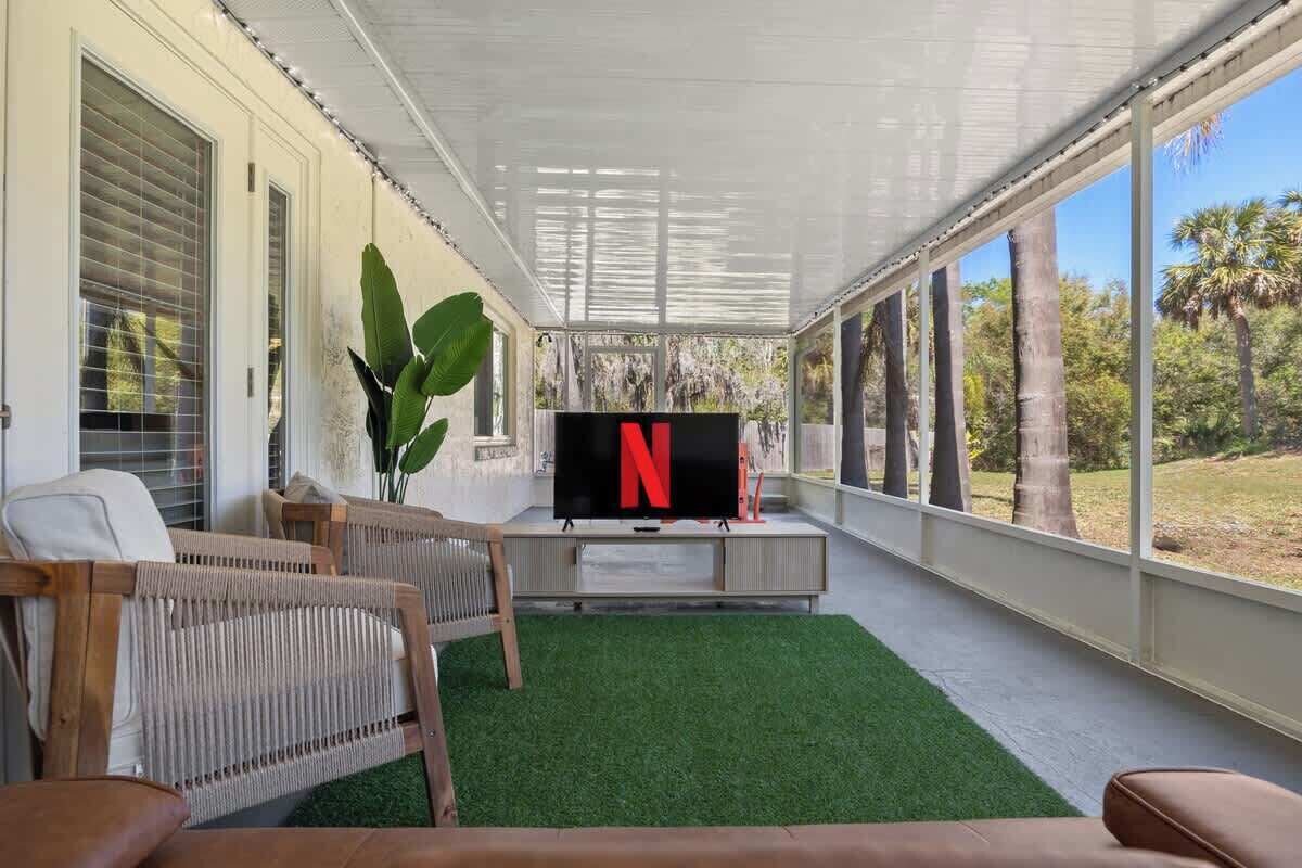 Un espacio al aire libre techado con una televisión, asientos y vistas a árboles.
