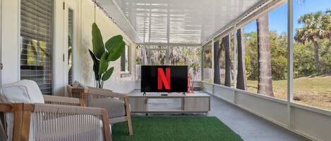Un espacio al aire libre techado con una televisión, asientos y vistas a árboles.