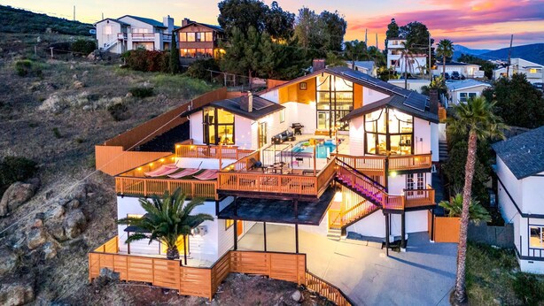 Ein modernes, mehrgeschossiges Haus mit einer großen Terrasse, einem Swimmingpool und einer Treppe, die zu den oberen Stockwerken führt.