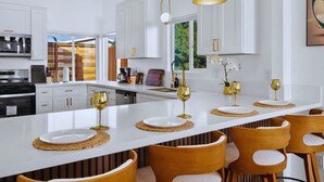 Eine moderne Küche mit weißen Schränken, einer zentralen Kochinsel mit goldenen Akzenten und Pendelleuchten.