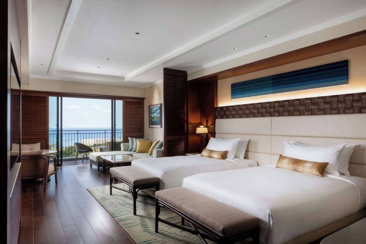 A hotel room with two beds, a balcony with a view, and a large window.