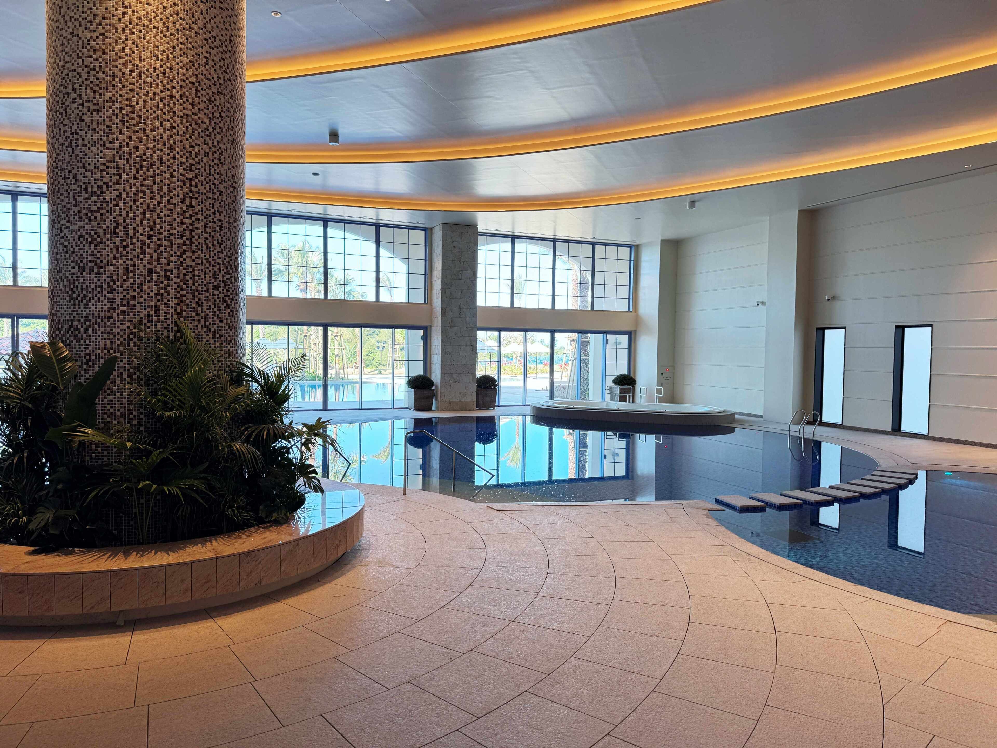 A spacious lobby with a large column, a pool area, and large windows.