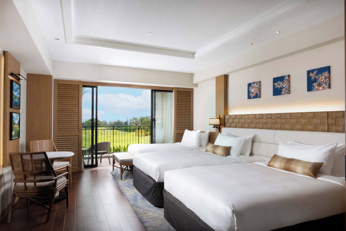 A hotel room with two beds, a balcony, a dining area with chairs, and artwork on the walls.