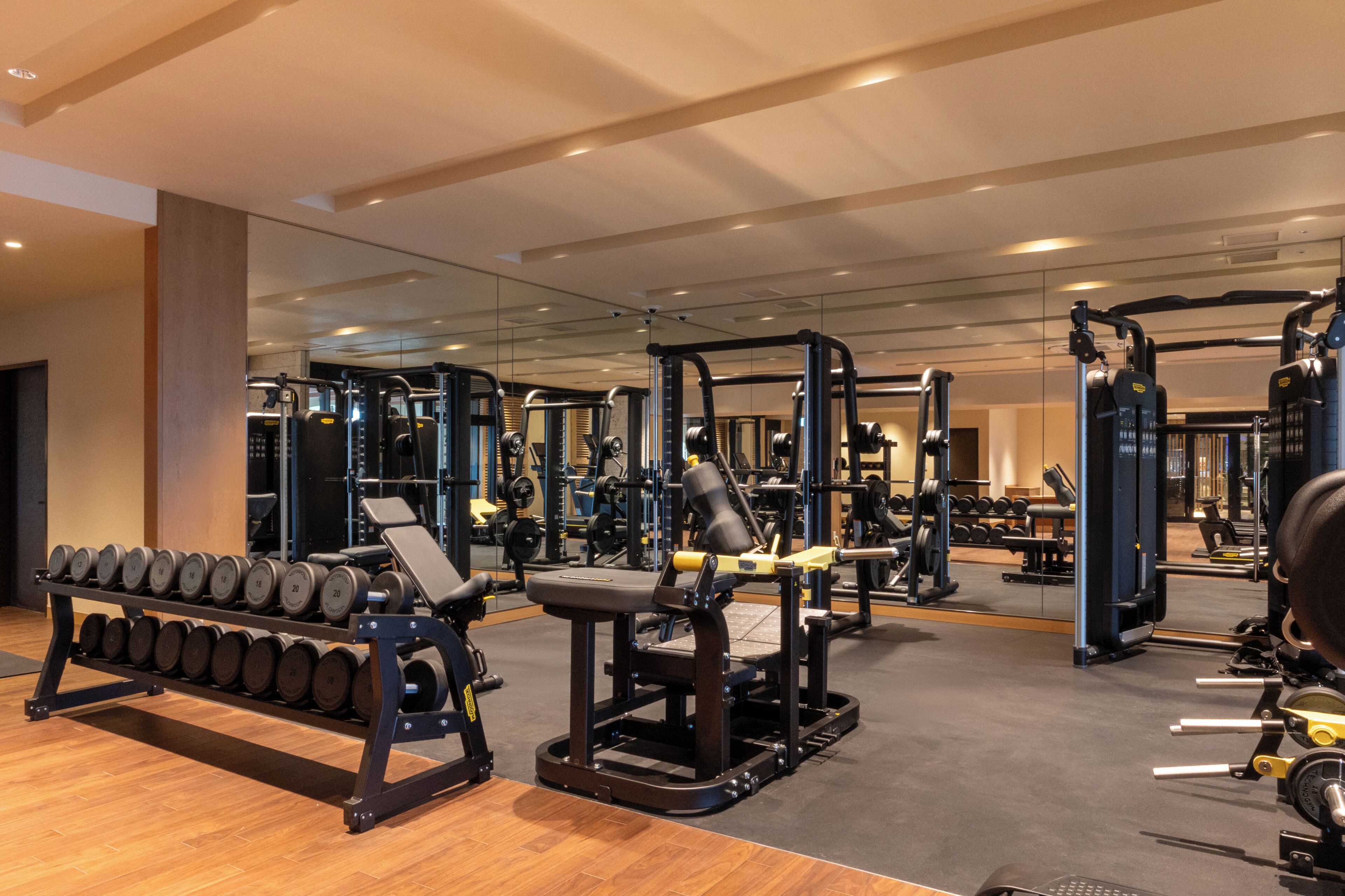 A gym with various exercise equipment, a rack of dumbbells, and a mirror reflecting the equipment.