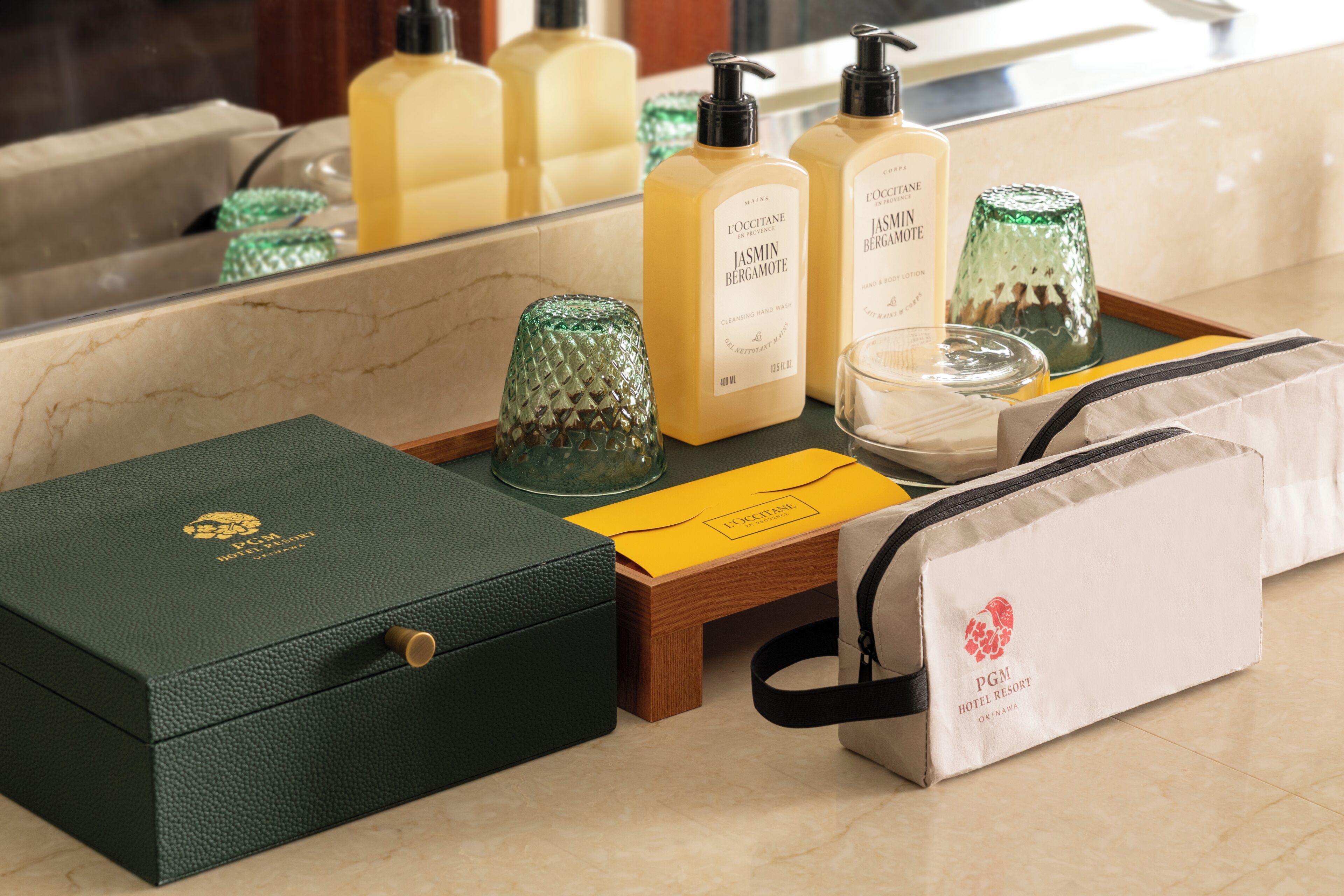 A bathroom vanity with toiletries, a green box, and a white bag with a logo.