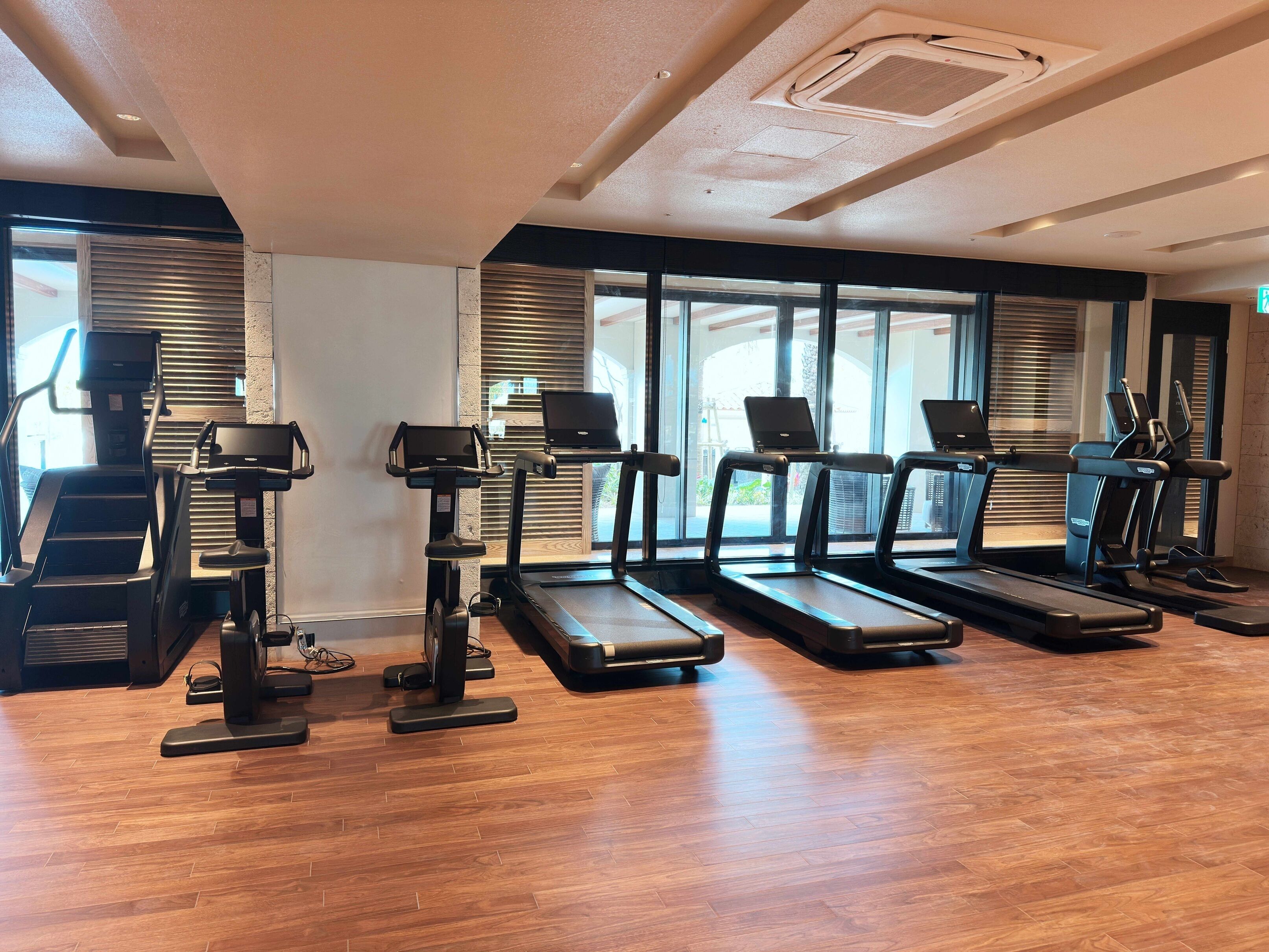 Un gimnasio con cintas de correr, elípticas y suelo de madera.