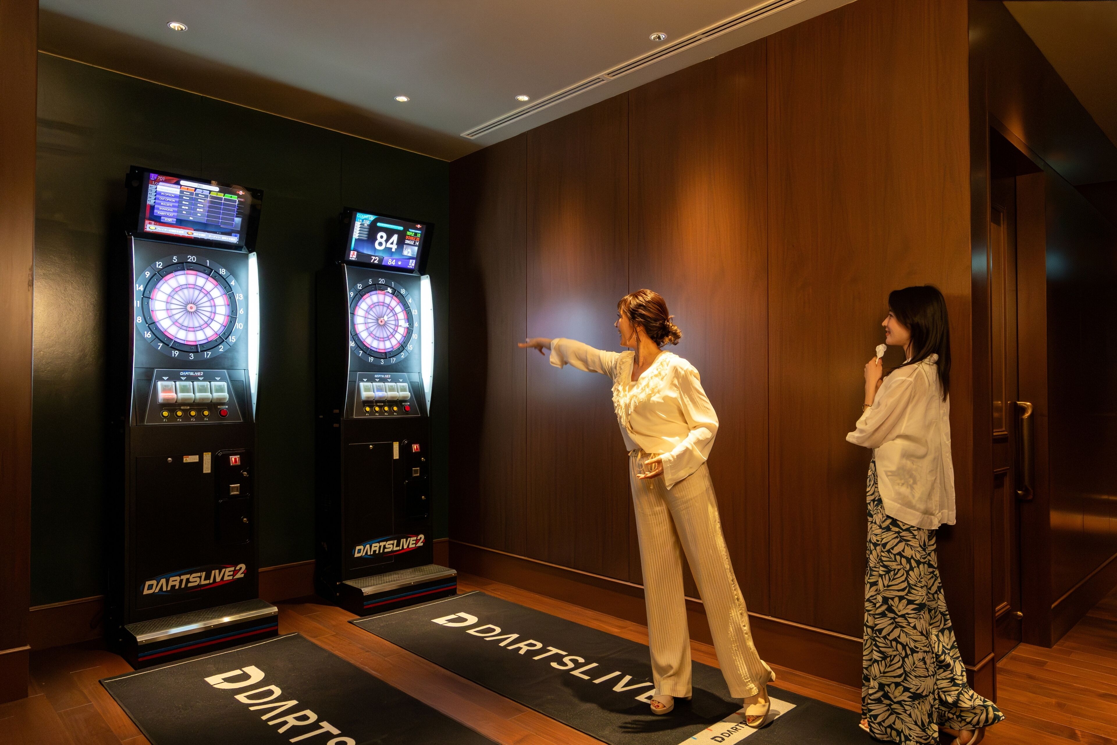 Two dartboards labeled 'DartsLive 2' in a room with wooden walls and a door.
