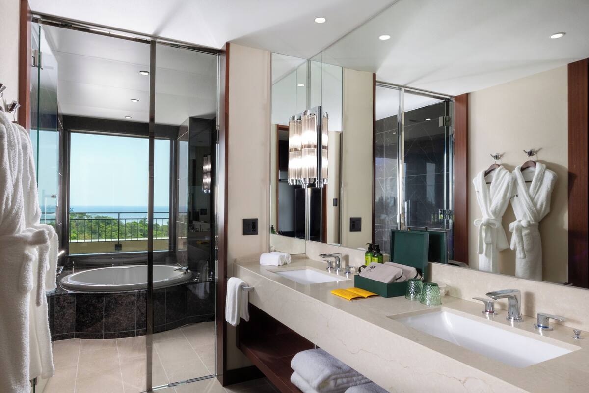 A modern bathroom with a large mirror, two sinks, a bathtub, and a glass-enclosed shower.