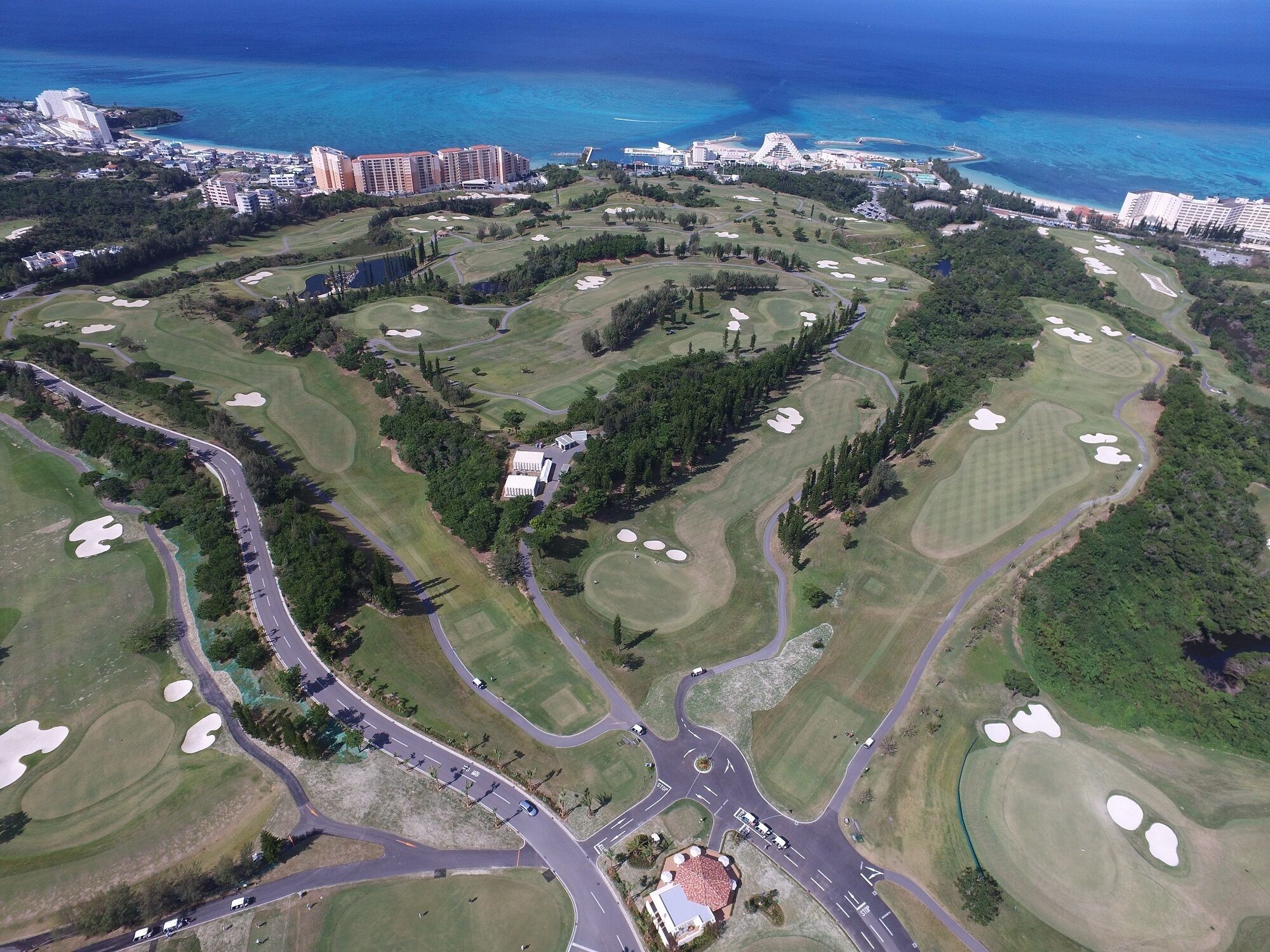 Vista aérea de un campo de golf con varios búnkeres, una casa club central y edificios residenciales circundantes.