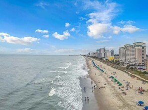 A coastal beach with buildings along the shore, a sandy beach, and the ocean.