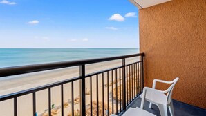 Un balcon donnant sur la plage, une chaise en plastique blanche et un mur à la texture particulière.