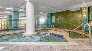 Un espace piscine intérieure doté d’une colonne centrale, d’un jacuzzi et d’un mur végétal.