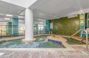 An indoor pool area with a central column, a hot tub, and a green wall.