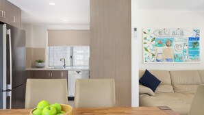 Una cocina moderna con comedor, un sofá color beige y una obra de arte titulada "BEACH HOUSE".