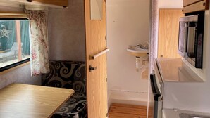 A compact RV interior with a wooden table, a small sink, and a window with curtains. - Glamping Casita RV on the Backbone with Stunning Views All Around (Fischer)