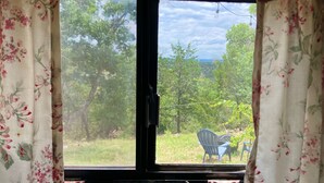 A room with a large window, a view of greenery outside, and a chair visible through the window. - Glamping Casita RV on the Backbone with Stunning Views All Around (Fischer)
