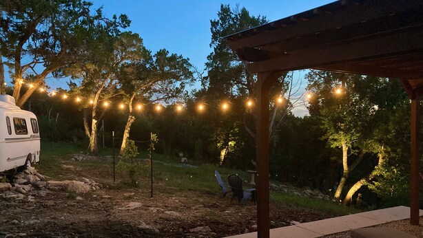 A covered outdoor area with string lights, a bench, and a white RV parked nearby. - Glamping Casita RV on the Backbone with Stunning Views All Around (Fischer)