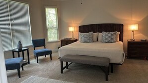 A bedroom with a large bed, two bedside tables, a chair, a bench, and two windows with blinds. - Woodlands House. 8 People, Restaurants, Movie Theater, HEB, Parks and Walkways. (Tomball)