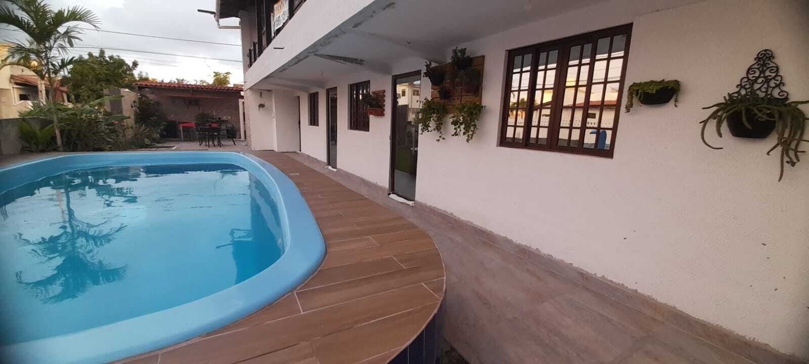 Una piscina adiacente a un edificio con terrazza piastrellata, piante in vaso e una finestra con un motivo a griglia.