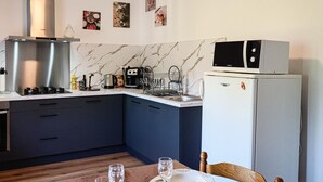 Et kompakt køkken med komfur, mikroovn og køleskab. Der er et spisebord med tallerkener og glas.