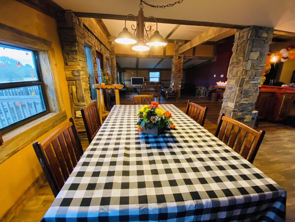 Un coin repas avec une nappe à carreaux, des chaises en bois, un vase de fleurs, des murs en pierre et une vue par la fenêtre.