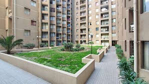 Un edificio residenziale a più piani con balconi, un cortile centrale con erba e piante, e un percorso pedonale in piastrelle.