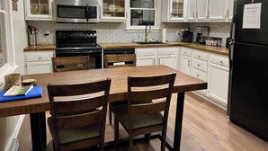 A kitchen with white cabinets, a black refrigerator, a wooden dining table with chairs, and a sign that says "LAKE". - Charming 3-bedroom House on 1 acre in Deep Creek (Oakland)