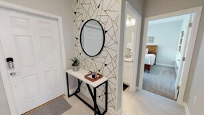 A hallway with a white door, a console table with a mirror, and a geometric wall design.