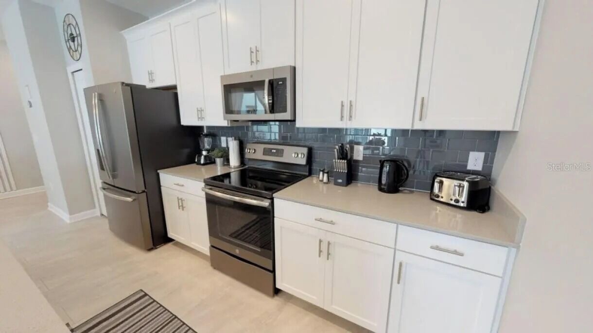 A modern kitchen with white cabinets, stainless steel appliances, and a tiled backsplash.