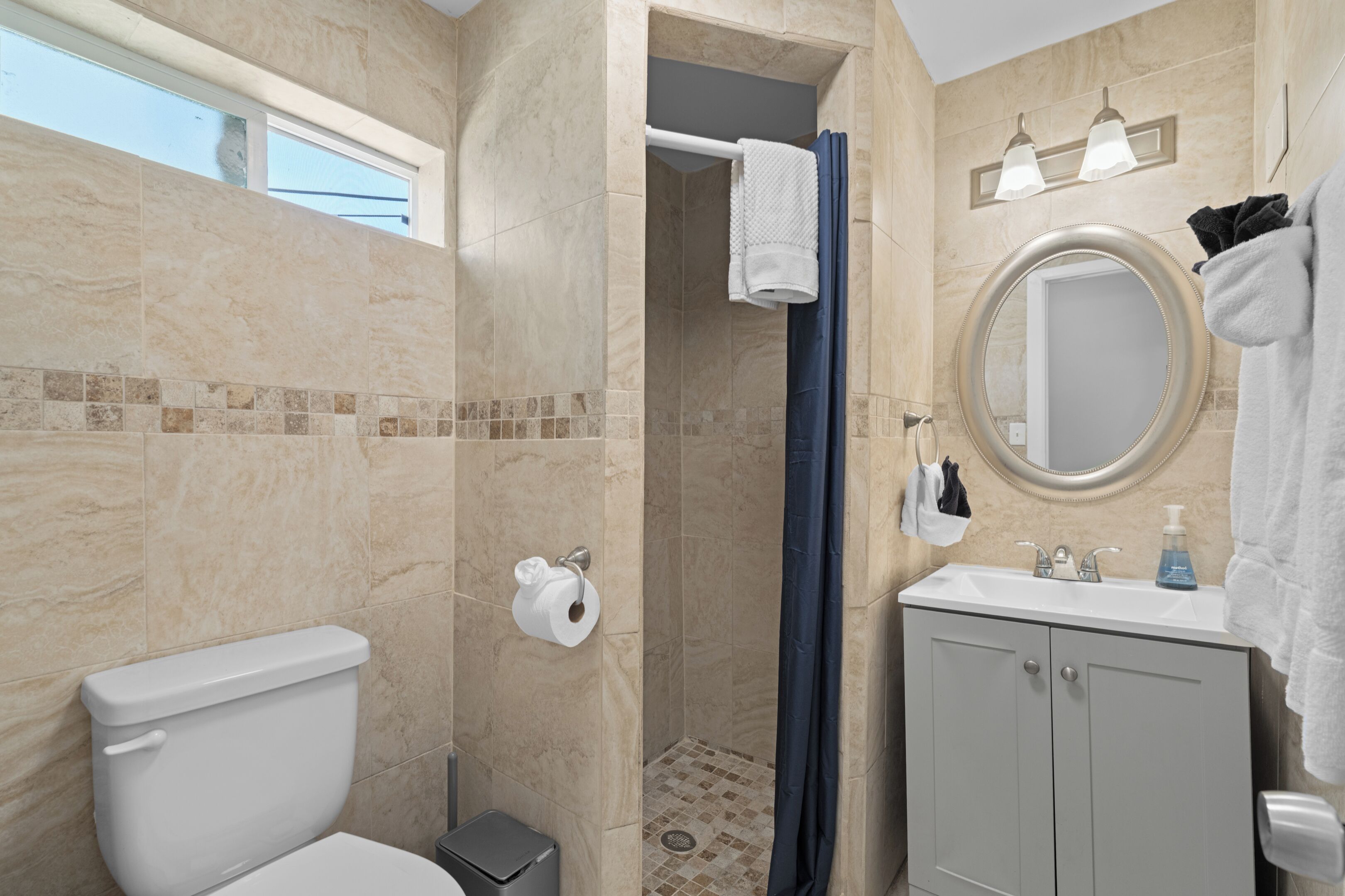 A bathroom with a toilet, shower, sink, and mirror.